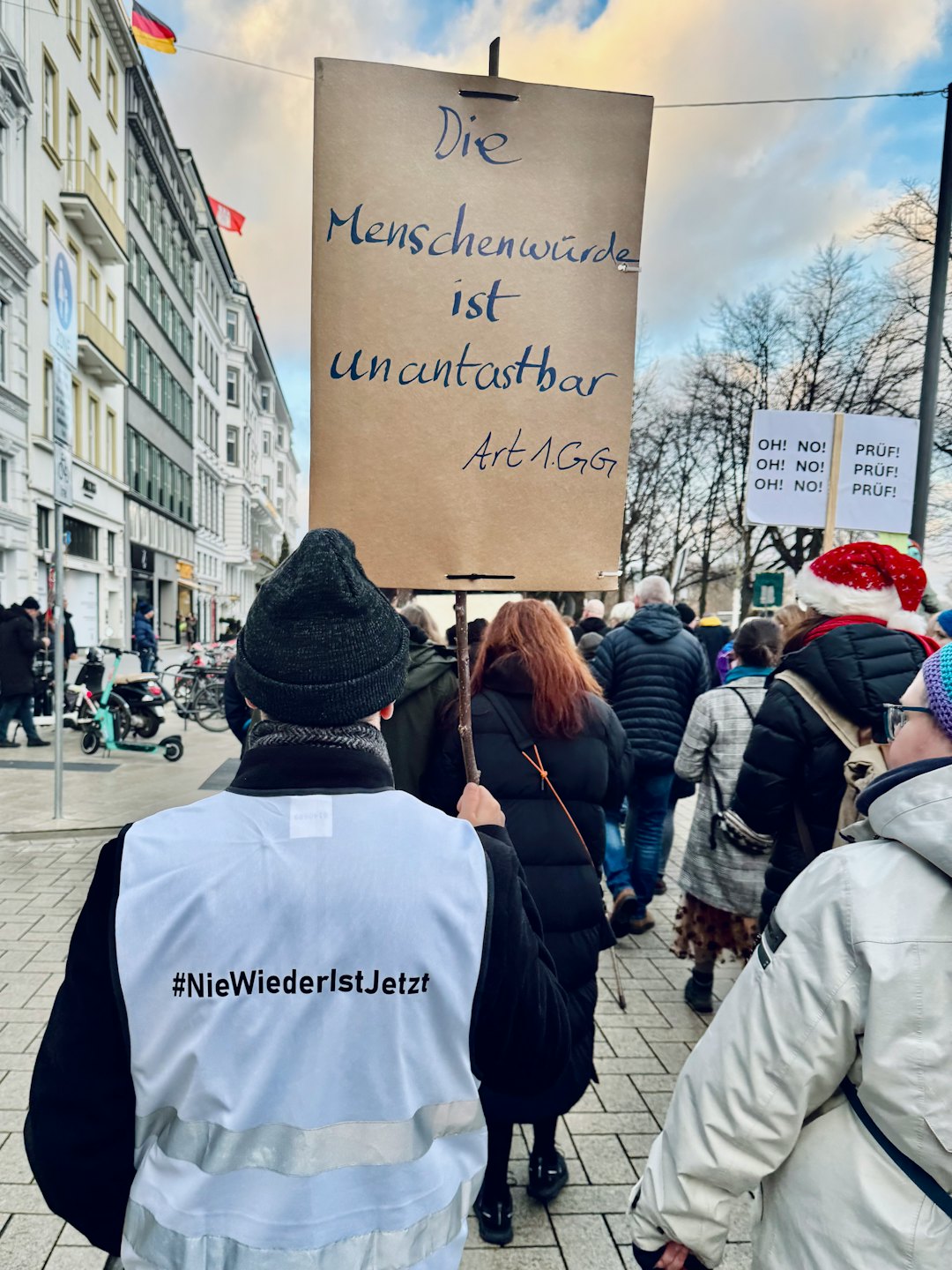 Demonstranten mit Plakaten gehen an Stadtgebäuden vorbei eine Straße entlang.