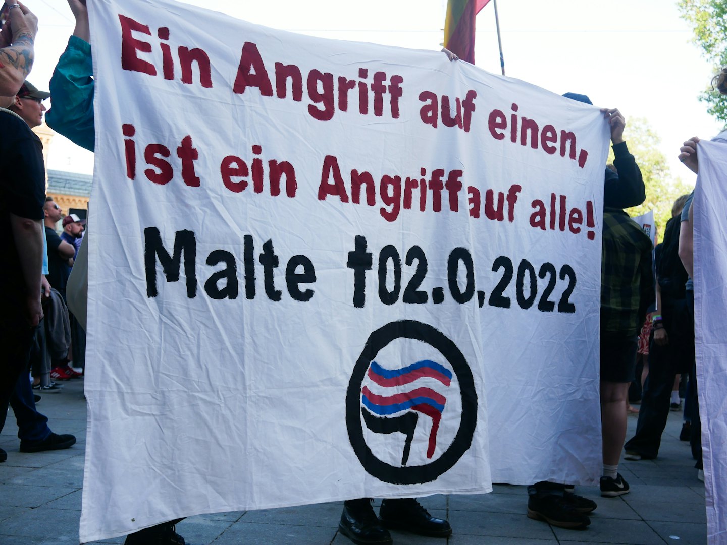 Demonstranten halten ein großes weißes Banner mit deutscher Aufschrift im Freien.