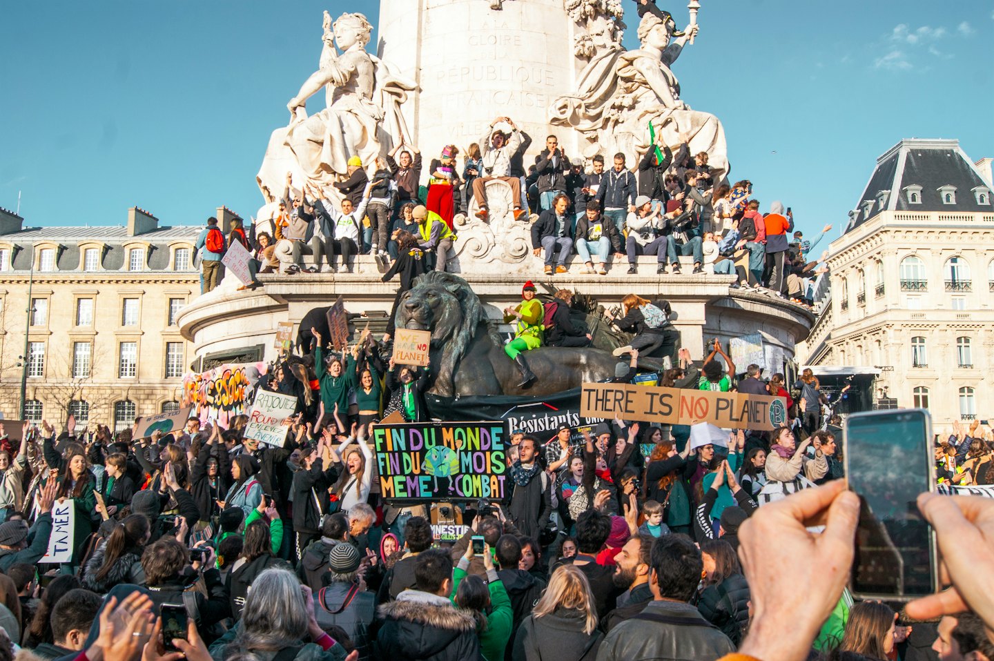 Vielfältige Demonstranten halten Schilder auf einem öffentlichen Platz in der Nähe eines Steindenkmals.