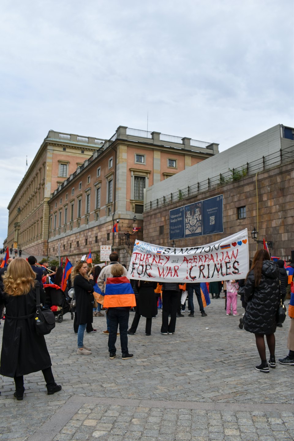 Demonstranten halten ein Banner vor einem pfirsichfarbenen Gebäude.