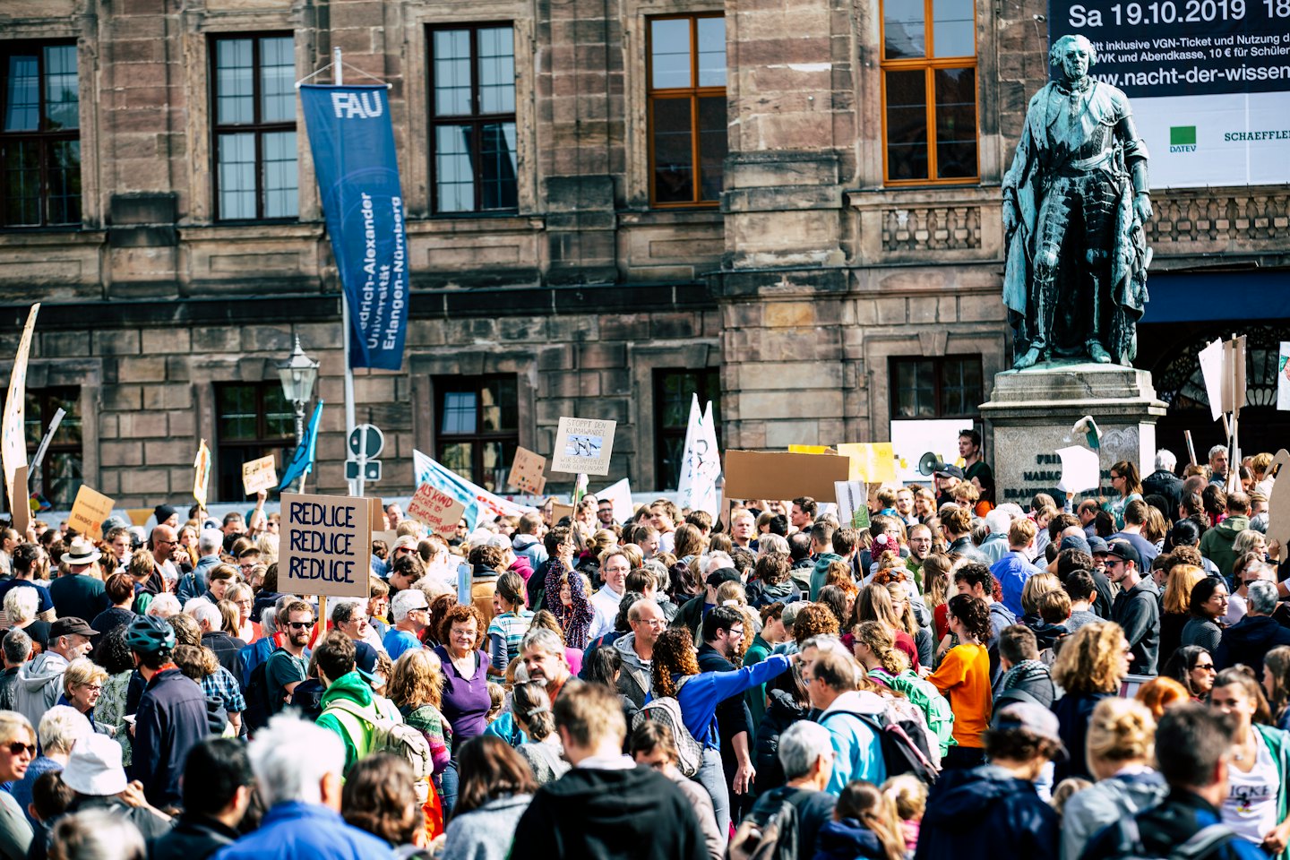 Menschen protestieren mit Schildern auf einem Stadtplatz gegen den Klimawandel.